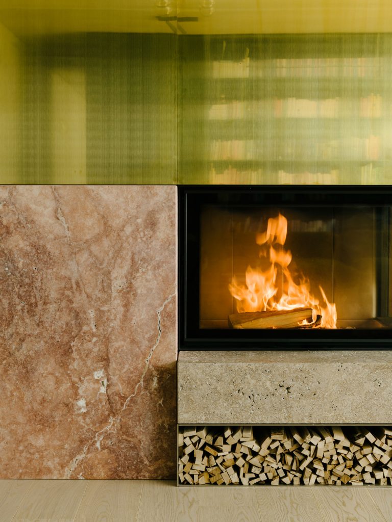 The Living Room occupies the space between an existing wall and the green box. The hearth is made from travertine Sierra ebru stone, red travertine, brass, and thin plates of stainless steel. Te design strategy is to create relationship between boxes. Photo ©Robert Rieger, Courtesy of Ester Bruzkus Architekten.