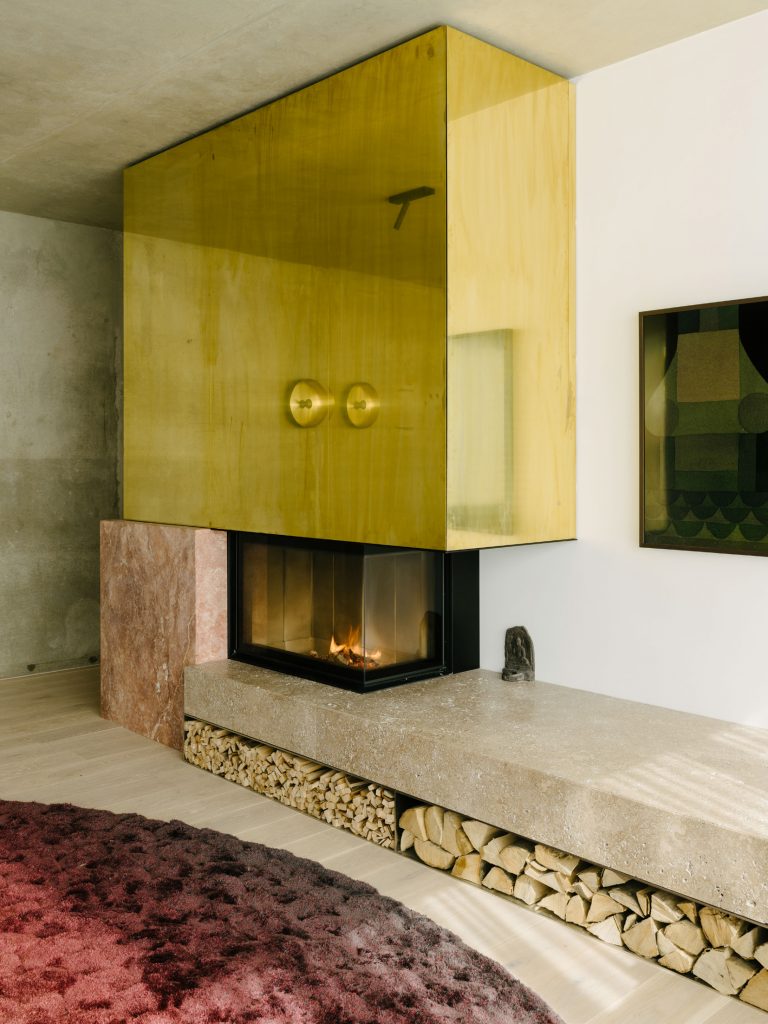 The Living Room occupies the space between an existing wall and the green box. The hearth is made from travertine Sierra ebru stone, red travertine, brass, and thin plates of stainless steel. Te design strategy is to create relationship between boxes. Photo ©Robert Rieger, Courtesy of Ester Bruzkus Architekten.