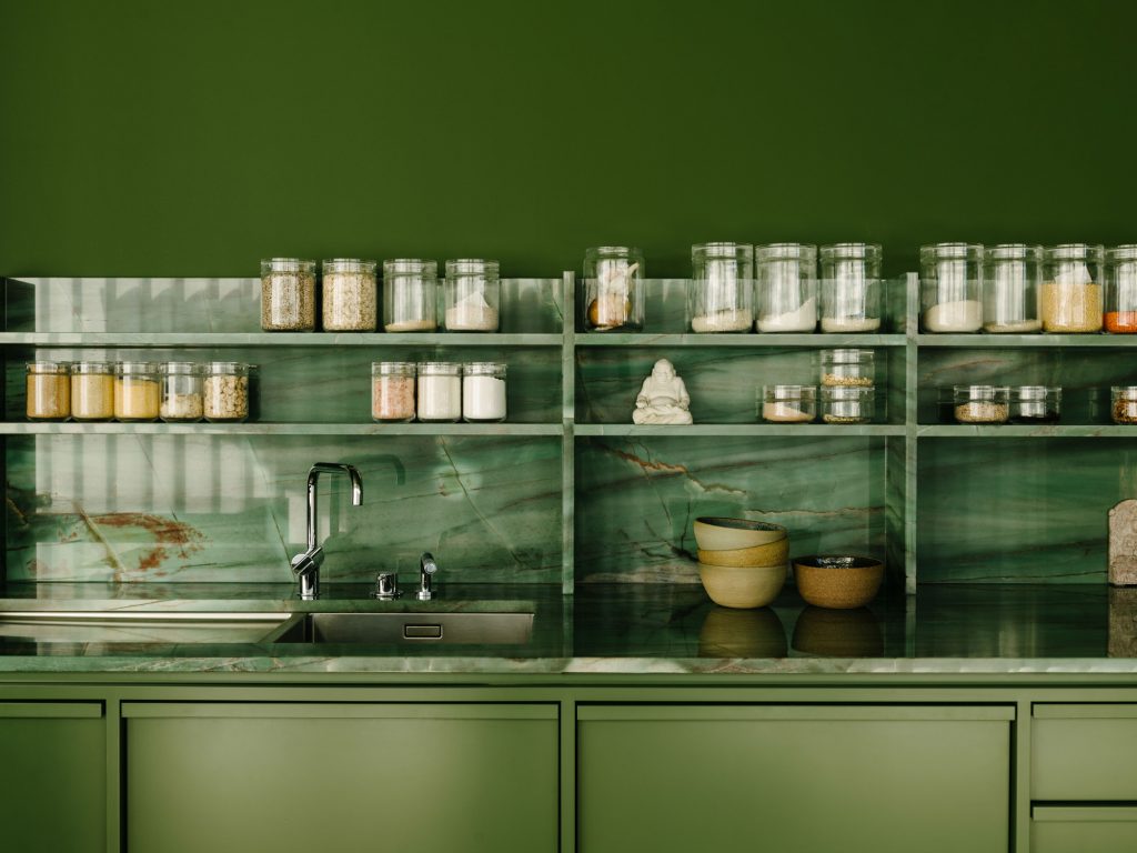 The kitchen counter, back and shelving are made from natural greenand- violet quartzite. The millwork on the green box is lacquered wood, some of which is detailed to have a strong rhythm of ribs. Photo ©Robert Rieger, Courtesy of Ester Bruzkus Architekten.