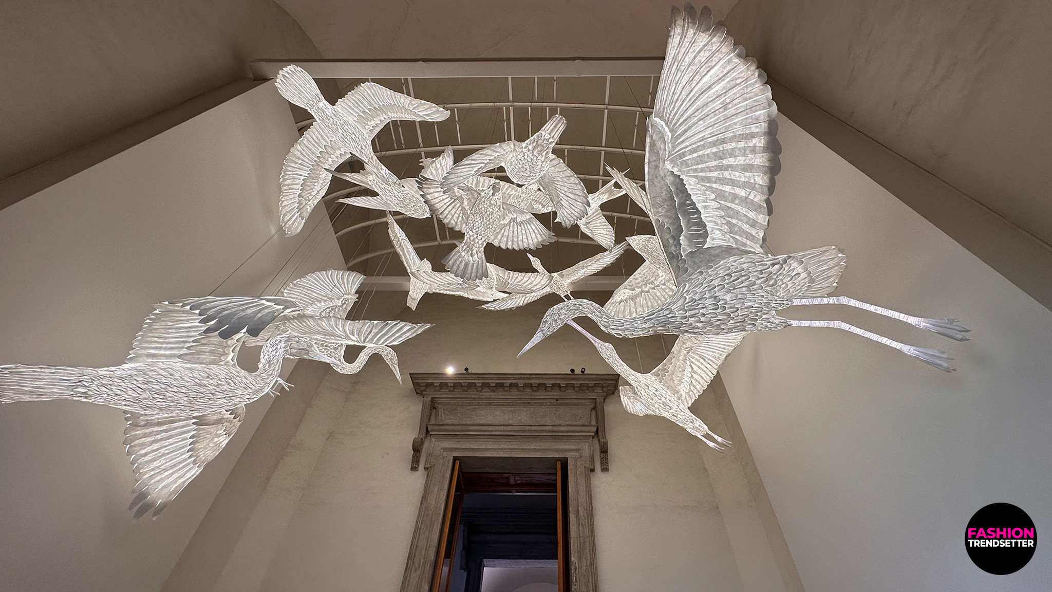 Homo Faber 2026: An Island of Light - "A Luminous Ark" by QIUWEN WEN Suspended above the staircase, A Luminous Ark celebrated the delicate beauty of paper through an enchanting assembly of illuminated bird sculptures. Created by Chinese artist Wen Qiuwen, the installation drew on Es Devlin's sketches of Venetian birds, translating their forms into graceful paper creations. Kestrels, egrets, herons, terns, and other winged inhabitants of the Venetian landscape appeared to float in the air, their translucent forms glowing like lanterns. Blending artistic interpretation with the poetic qualities of light and material, the installation paid tribute to Venice's natural heritage and the remarkable potential of paper as a medium for sculptural expression...Learn more. Photo © 2026, Senay Gokcen for Fashion Trendsetter.