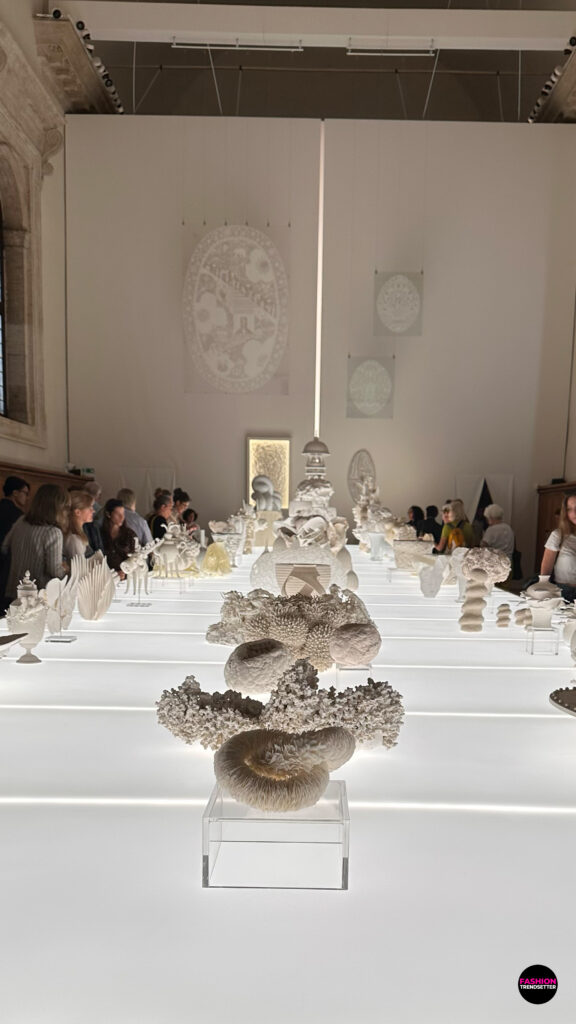 Homo Faber 2026: An Island of Light - A Feast of Light A Feast of Light explored the transformative power of light through the delicate interplay of translucency, material, and form. Within the magnificent Palladian Refectory, a vertical line of light divided the space, illuminating a curated collection of white objects and revealing the subtle qualities of their surfaces. Delicate paper cuttings were displayed above a lightbox table featuring sculptural works in porcelain, glass, textiles, paper, and other materials. United by a restrained monochromatic palette, these creations demonstrated how light could reveal intricate details, soften contours, and lend materials an almost ethereal presence. Behind the wall, an extraordinary reproduction of Paolo Veronese's The Wedding at Cana offered a striking artistic counterpoint, connecting the contemporary celebration of craftsmanship with the grandeur of Venetian art. Photos © 2026, Senay Gokcen for Fashion Trendsetter.